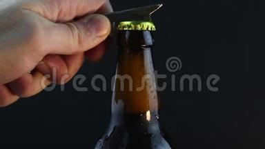 酒保打开一瓶雾蒙蒙的黑啤酒。 一个年轻人的手打开一瓶又冷又黑的啤酒。